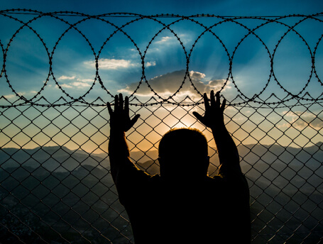 Prisoner watches sunset from behind a barbed wire prison fence